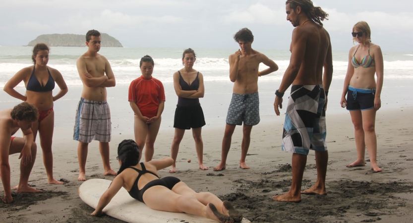 a group of people watch someone demonstrating a surfing technique on a surf board resting on the sand